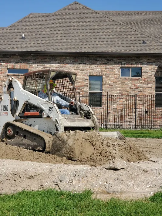 Compact loader excavating soil beside a house